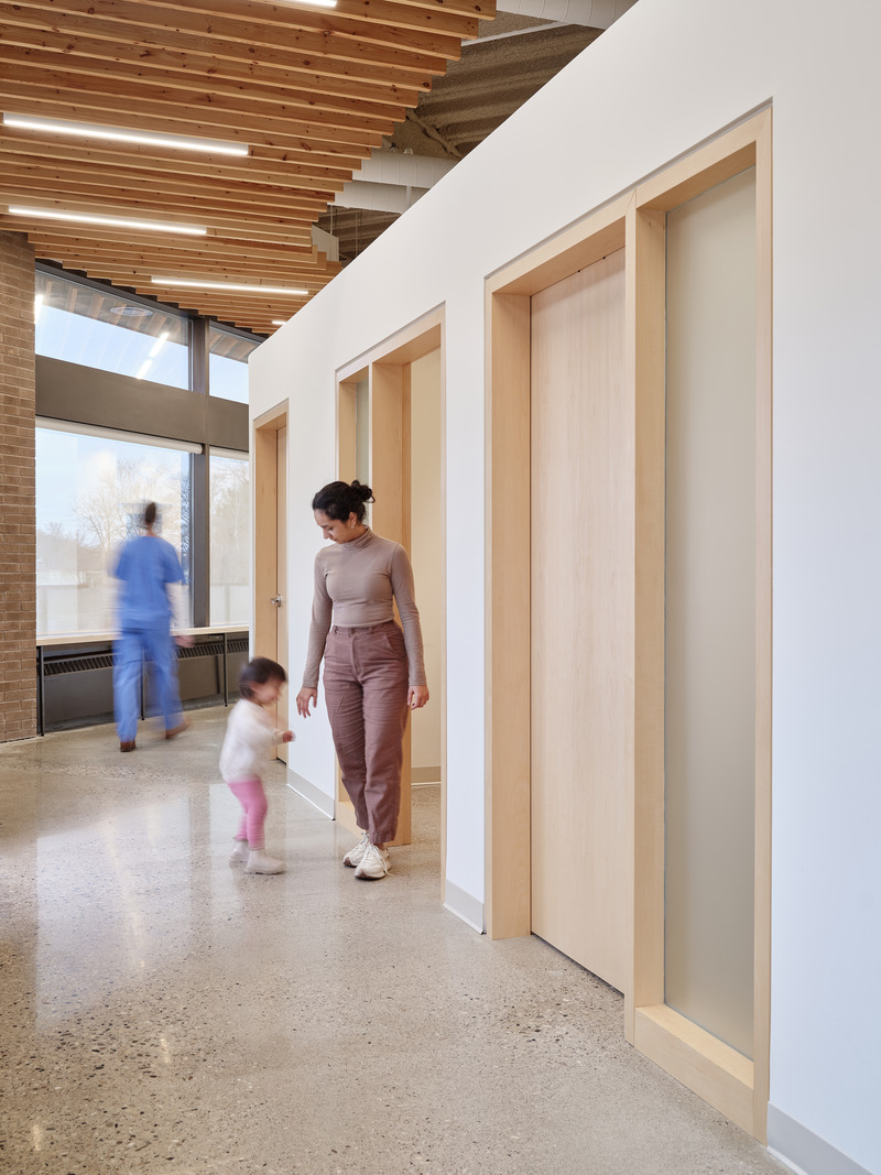 Dossier de presse | 7540-01 - Communiqué de presse | Galt Health - Fonseka Studio - Architecture commerciale - Un corridor généreux et baigné de lumière mène à une rangée de salles de patients, s'incurvant vers la zone privée, offrant au personnel et aux médecins un chemin continu et circulaire à travers la clinique. Un plafond à lattes de bois dissimule les services du bâtiment sans limiter la hauteur perçue de l'espace. - Crédit photo : Riley Snelling