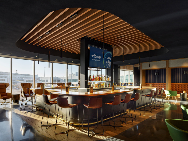 Dossier de presse | 2757-47 - Communiqué de presse | William Duff Architects (WDA) Blends Brand Identity with Bay Area Creativity for Alaska Airlines - William Duff Architects (WDA) - Design d’intérieur commercial -  In the "Cut Loose" area, which features a rounded bar, seating options include bar stools, runway-side high back chairs, banquettes and club chairs.  - Crédit photo : Matthew Millman