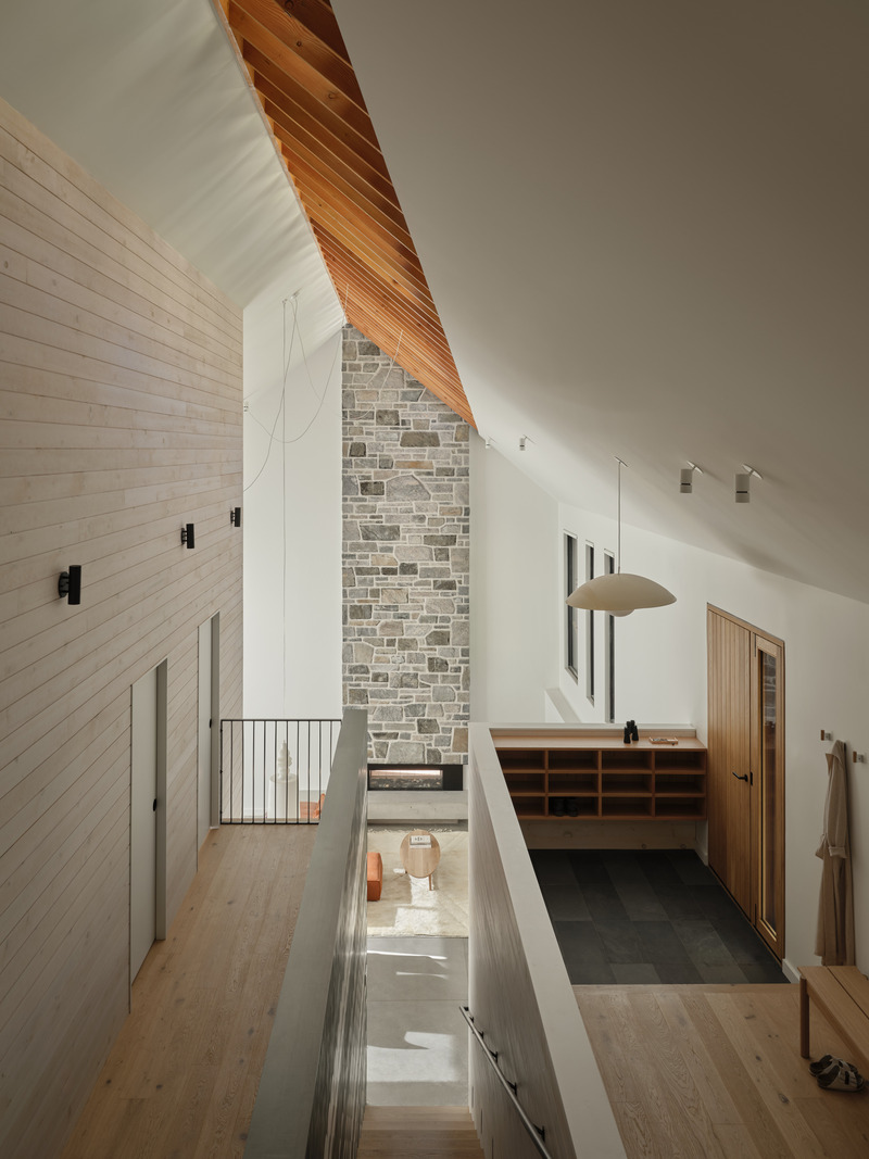 Press kit | 7600-02 - Press release | Shield and Shelter: An Embracing Lakeside Family Retreat that Opens Intimately and Sensitively to its Untamed Surroundings in the Heart of the Muskoka Region - Barbora Vokac Taylor Architect Inc. (BVT A) - Residential Architecture -  View from the loft: A dramatic floor-to-ceiling stone chimney marks the division between the house proper and the outdoor Muskoka Room and anchors the double-height space.  - Photo credit: Doublespace
