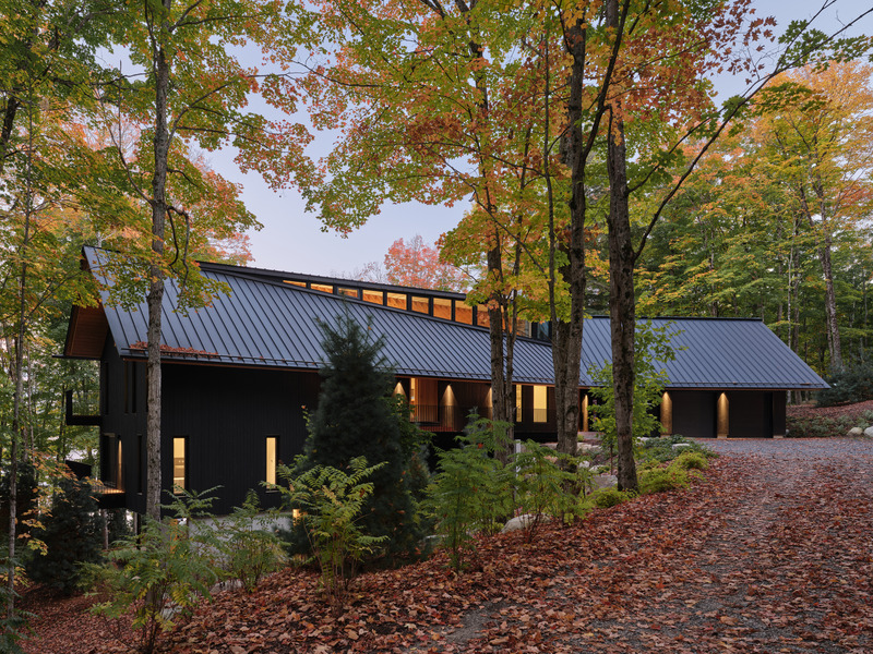 Press kit | 7600-02 - Press release | Shield and Shelter: An Embracing Lakeside Family Retreat that Opens Intimately and Sensitively to its Untamed Surroundings in the Heart of the Muskoka Region - Barbora Vokac Taylor Architect Inc. (BVT A) - Residential Architecture -  View from the road:  A single, low-slung black roof covers both cedar-clad volumes, peeled back at the top for the installation of a series of clerestory windows that welcome sunlight and gentle breezes into the heart of the home.  - Photo credit: Doublespace