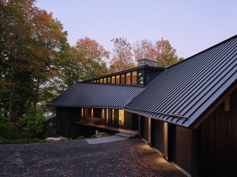 Press kit | 7600-02 - Press release | Shield and Shelter: An Embracing Lakeside Family Retreat that Opens Intimately and Sensitively to its Untamed Surroundings in the Heart of the Muskoka Region - Barbora Vokac Taylor Architect Inc. (BVT A) - Residential Architecture -  <p>View from the driveway: Deep overhangs extend from the sloped black zinc roof that serve as shelter as one roams the exterior edges of the cottage. </p><br><p>The clerestorey windows peel and bend from the roof form, cracking open to allow light to filter through, illuminating and revealing the exposed structure and the quality of the natural materials.</p>  - Photo credit: Doublespace