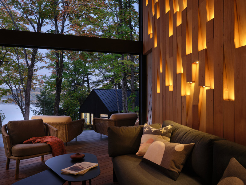 Press kit | 7600-02 - Press release | Shield and Shelter: An Embracing Lakeside Family Retreat that Opens Intimately and Sensitively to its Untamed Surroundings in the Heart of the Muskoka Region - Barbora Vokac Taylor Architect Inc. (BVT A) - Residential Architecture -  View from Muskoka room - bunkie in the distance: Clean exterior lines contrast with the rugged landscape, while inside, textured cedar walls fold and split revealing lights that both invite and highlight the raw materials.  - Photo credit: Doublespace
