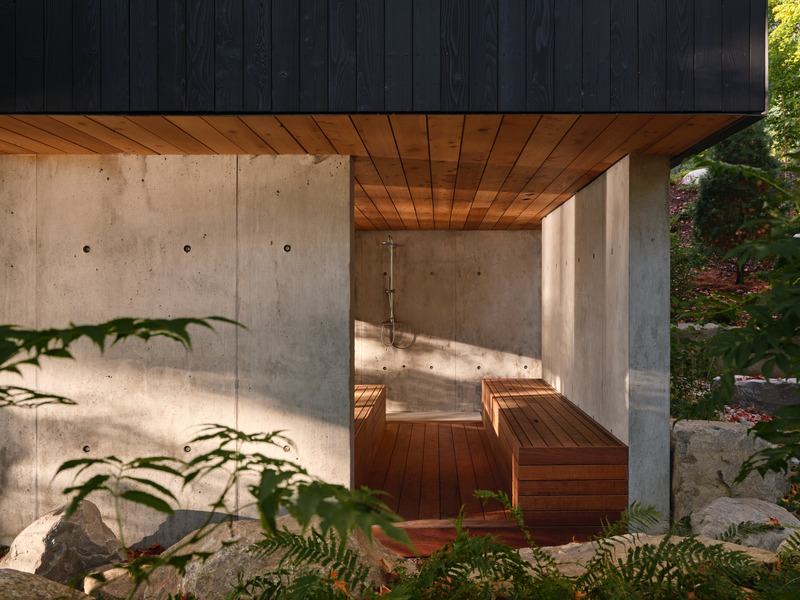 Press kit | 7600-02 - Press release | Shield and Shelter: An Embracing Lakeside Family Retreat that Opens Intimately and Sensitively to its Untamed Surroundings in the Heart of the Muskoka Region - Barbora Vokac Taylor Architect Inc. (BVT A) - Residential Architecture -  The lowest-level, a basement walkout, includes a sauna and wet bar. Just outdoors, a covered hot tub sits below the overhang with a cedar-clad ceiling, surrounded by trees and nestled into the landscape. Architectural poured concrete walls both support the structure above and screen off the space for privacy, while framing views of the surrounding forest and lake.  - Photo credit: Doublespace