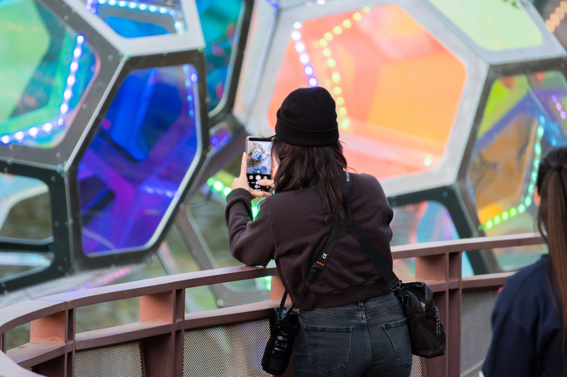Press kit | 5595-10 - Press release | Molecules: A Series of Interactive Water Molecules Rising up from the Arizona Canal, Sparking a Connection Between Visitors and the Surrounding Environment Through Light and Sound - The Urban Conga - Multimedia Design - A women takes a photo of herself reflected onto the side of one of the Molecules.  - Photo credit: Charles Darr