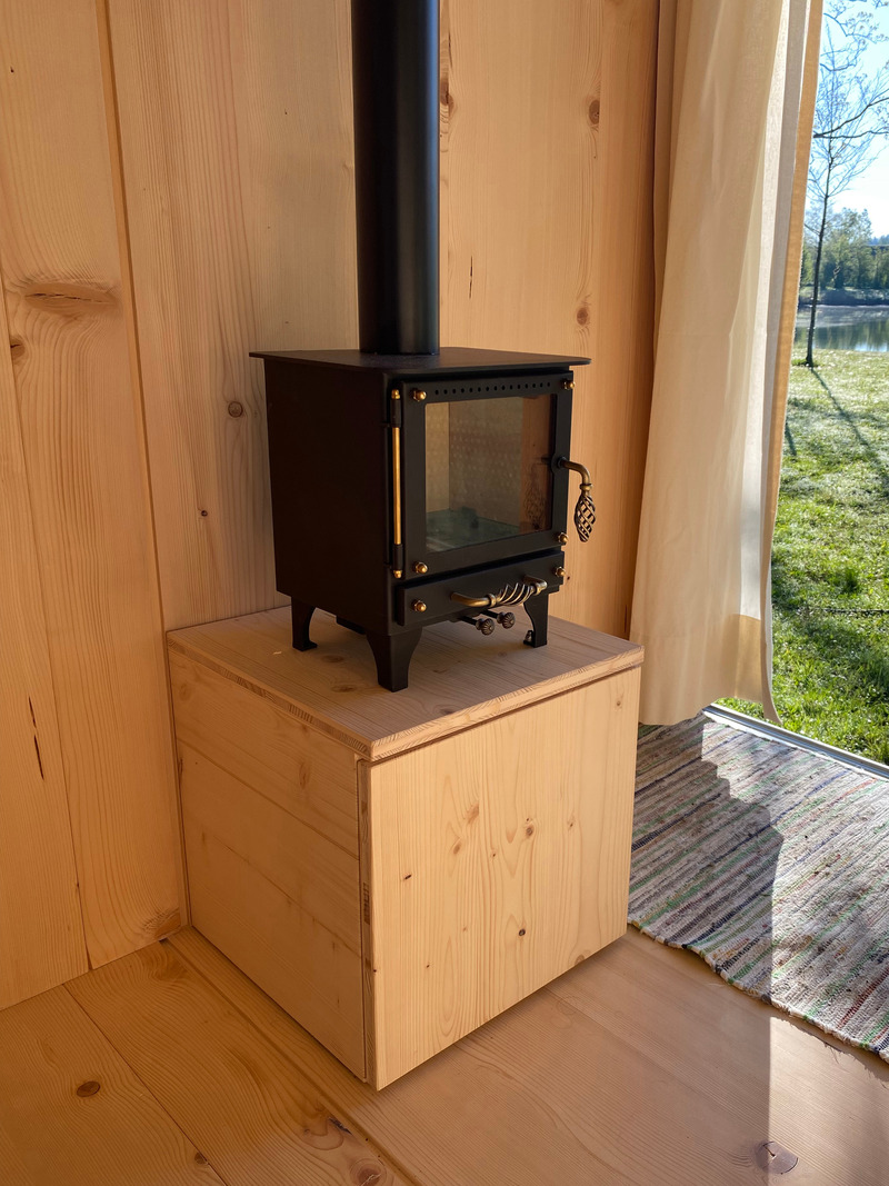 Press kit | 7649-02 - Press release | COCOON Freelancer -  Free of Glue, Chemicals and Plastic - AttiaDesign & Weidlich moon-wood manufactory - Lifestyle -  Equipped with TinyStove: Featuring a 3 kW TinyStove with integrated wood storage and an external air intake to ensure clean combustion while maintaining excellent indoor air quality. (Note: The storage and transformable table are still prototypes made from glued wood, currently being tested for usability.) - Photo credit: AttiaDesign
