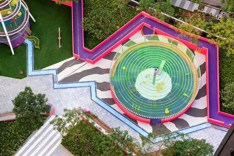 Dossier de presse | 5086-04 - Communiqué de presse | Les Résidences Buji par BAM : couleurs vives - Ballistic Architecture Machine - Architecture de paysage -  <p>Vue aérienne de la tente de jeu pour tout-petits des Résidences Buji, où un filet en tissu vert concentrique fait office d’abri ombragé sous les tours et où une vasque en caoutchouc violet renferme un bac à sable blanc.</p> - Crédit photo : Amey Kandalgaonkar