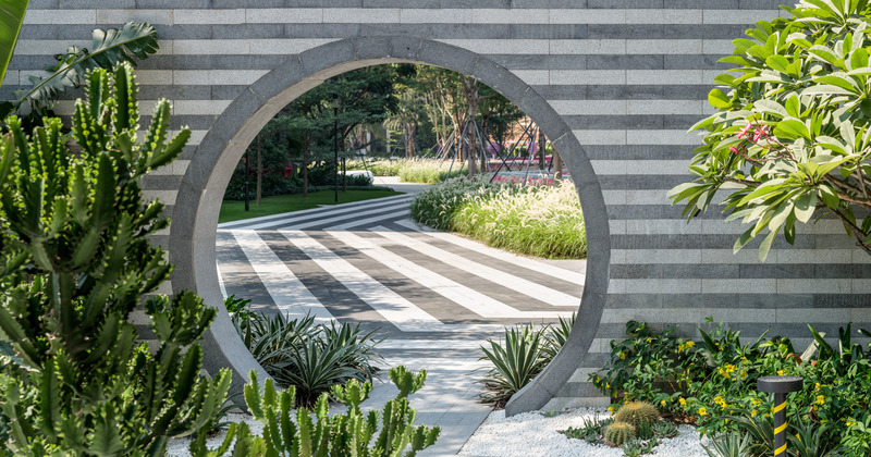 Dossier de presse | 5086-04 - Communiqué de presse | Les Résidences Buji par BAM : couleurs vives - Ballistic Architecture Machine - Architecture de paysage - <p>Vue à travers la porte lunaire rayée de gris et de blanc du jardin de cactus des Résidences Buji, où le portail circulaire encadre le pavement rayé, la végétation et un aperçu des murs roses au-delà.</p> - Crédit photo : Amey Kandalgaonkar