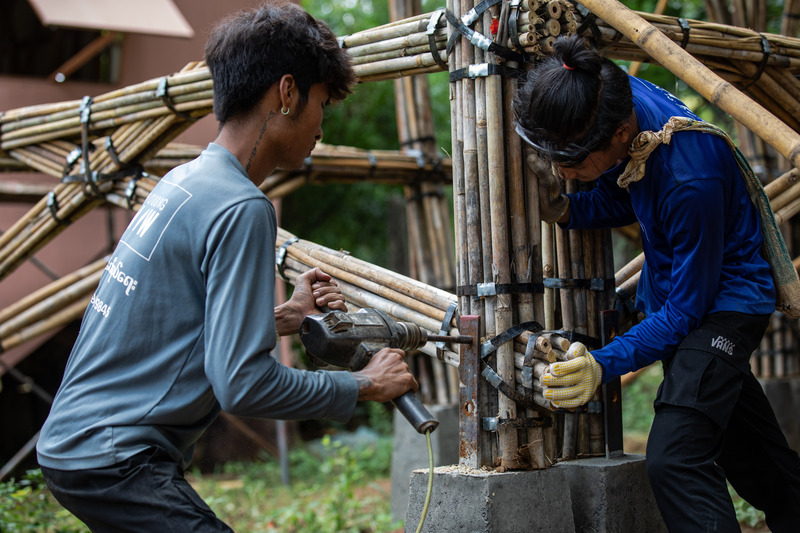 Press kit | 7035-02 - Press release | Bamboo Housing Resists 7.7 Earthquake in Conflict-Torn Myanmar, Built for Displaced Families - Blue Temple - Institutional Architecture - Two builders assembling a bamboo column footing, combining bundled culms with steel bracing. - Photo credit: Aung Htay Hlaing
