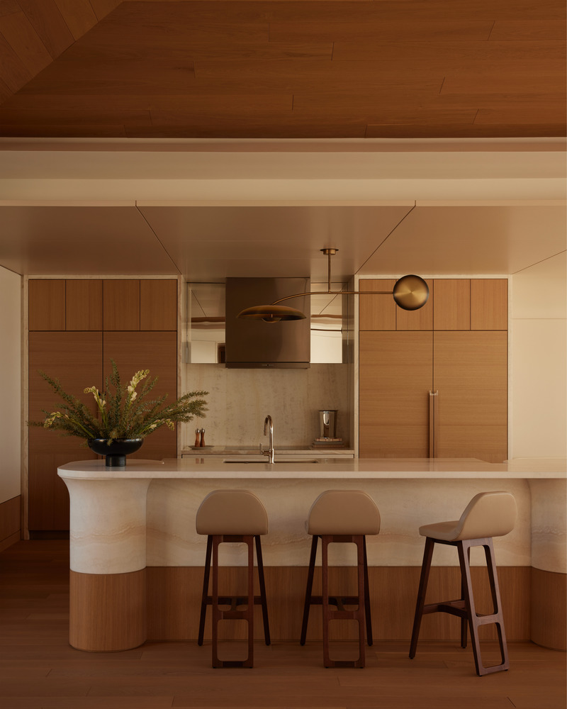 Press kit | 6087-07 - Press release | Study in Serenity: A Beachside Haven of Precision and Craftsmanship - Daniel Joseph Chenin - Residential Interior Design - The sculptural onyx island is designed in the round, its front serving as a refined workspace and room divider with integrated appliances and a concealed pop-up television, while its curved back transitions seamlessly into the living area as a bar. This duality blurs boundaries between utility and hospitality, reinforcing the home’s balance of function and elegance. - Photo credit: Tim Hirschmann