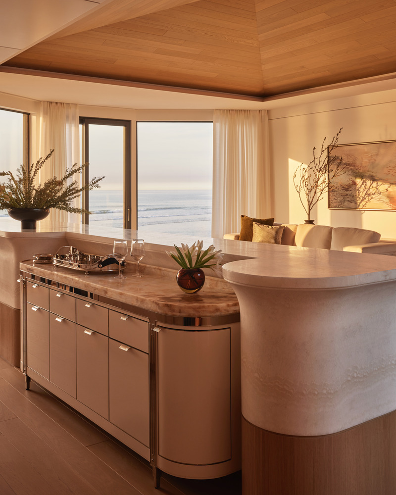 Press kit | 6087-07 - Press release | Study in Serenity: A Beachside Haven of Precision and Craftsmanship - Daniel Joseph Chenin - Residential Interior Design - The sculptural onyx island is designed in the round, its front serving as a refined workspace and room divider with integrated appliances and a concealed pop-up television, while its curved back transitions seamlessly into the living area as a bar. This duality blurs boundaries between utility and hospitality, reinforcing the home’s balance of function and elegance. - Photo credit: Tim Hirschmann