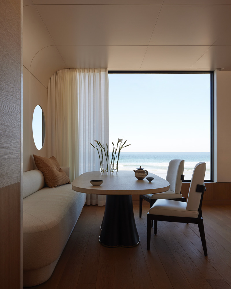 Press kit | 6087-07 - Press release | Study in Serenity: A Beachside Haven of Precision and Craftsmanship - Daniel Joseph Chenin - Residential Interior Design - The dining alcove recalls the intimacy of a yacht’s cabin, with a built-in banquette, circular port window, and panoramic glazing that frame the horizon like an ever-shifting seascape. - Photo credit: Tim Hirschmann