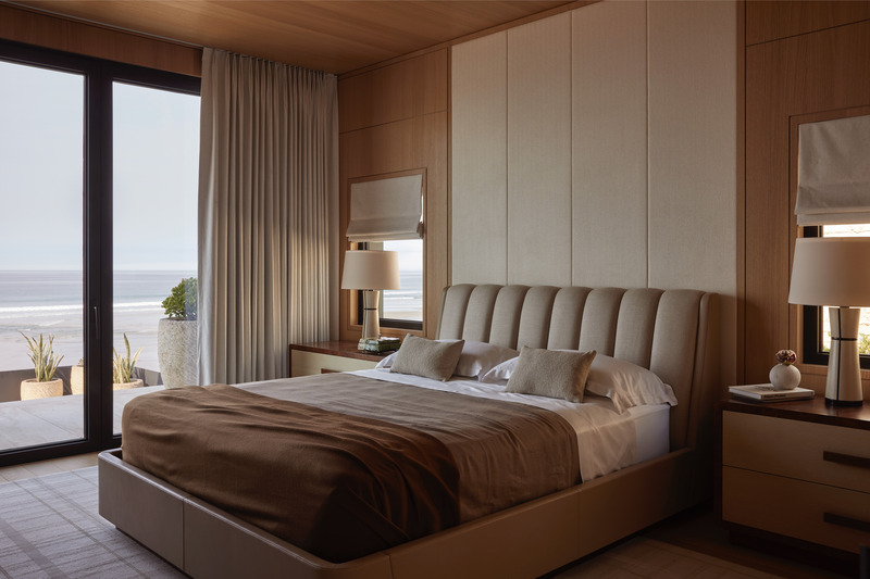 Press kit | 6087-07 - Press release | Study in Serenity: A Beachside Haven of Precision and Craftsmanship - Daniel Joseph Chenin - Residential Interior Design - The primary bedroom is wrapped in warm oak millwork and tailored textiles, framing expansive ocean views beyond. A sculptural light fixture floats above, adding a contemporary counterpoint to the serene palette of natural materials and soft coastal tones. - Photo credit: Tim Hirschmann