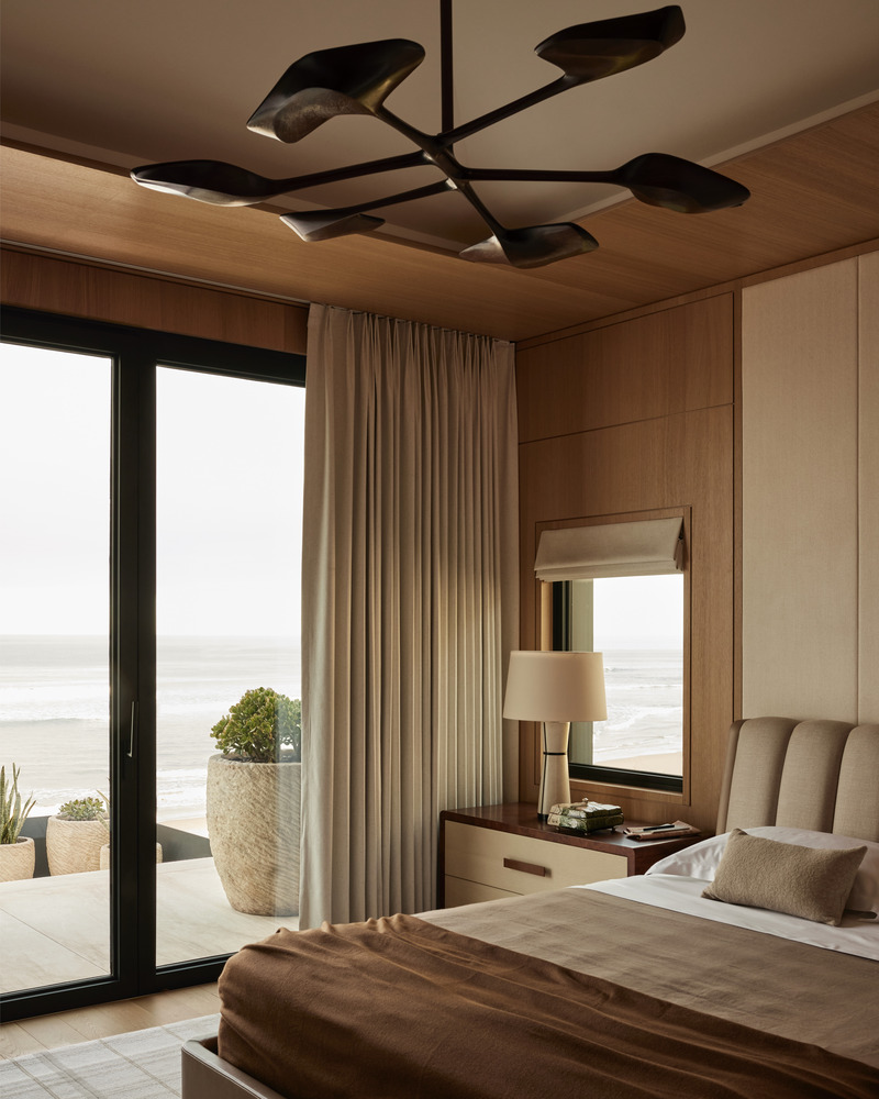 Press kit | 6087-07 - Press release | Study in Serenity: A Beachside Haven of Precision and Craftsmanship - Daniel Joseph Chenin - Residential Interior Design - The primary bedroom pairs oak millwork and tailored textiles with sweeping ocean views, while a sculptural light fixture by Thomas Newman Studios recalls kelp drifting on the water’s surface as seen from beneath, adding a lyrical counterpoint to the room’s serene composition. - Photo credit: Tim Hirschmann