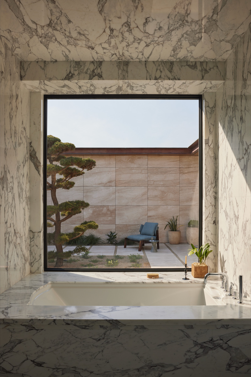 Press kit | 6087-07 - Press release | Study in Serenity: A Beachside Haven of Precision and Craftsmanship - Daniel Joseph Chenin - Residential Interior Design - Encased in veined marble, the soaking tub frames the courtyard beyond like a living artwork, where sculpted greenery and stone planes extend the serenity of the interior into the landscape. - Photo credit: Tim Hirschmann