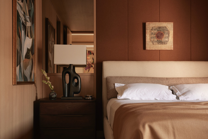 Press kit | 6087-07 - Press release | Study in Serenity: A Beachside Haven of Precision and Craftsmanship - Daniel Joseph Chenin - Residential Interior Design - A detail of the guest suite captures its quiet elegance: a sculptural black lamp anchors the walnut nightstand, while the upholstered headboard and sienna wall panels create a warm, enveloping backdrop accented by art with subtle geometric rhythm. - Photo credit: Tim Hirschmann