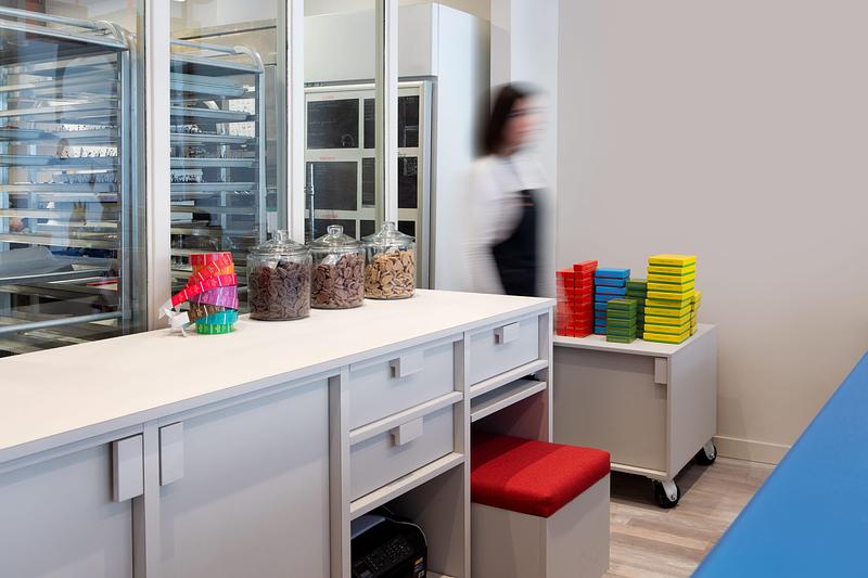 Dossier de presse | 1676-10 - Communiqué de presse | Réinventer la magie du chocolat : une collaboration réussie pour Les Chocolats de Chloé - ADHOC - Design d’intérieur commercial - Vitrage sépare la cuisine épurée du commerce coloré - Crédit photo : Vicky Rousseau