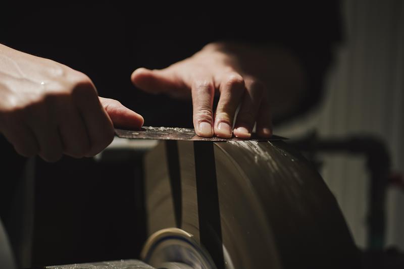 Dossier de presse | 7830-01 - Communiqué de presse | Tojiro Knife Gallery Osaka Wins Dezeen Award 2025 - KATATA YOSHIHITO DESIGN (L/O) - Design d’intérieur commercial - Close-up of hands preparing a knife during maintenance, showing the craft process in detail. - Crédit photo : Masaaki Inoue