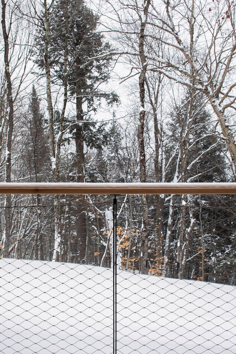 Press kit | 2054-05 - Press release | Laurentian Forest House - RobitailleCurtis - Residential Architecture - A detailed view through the custom-designed stainless steel mesh guardrail with a cedar handrail. - Photo credit: Adrien Williams