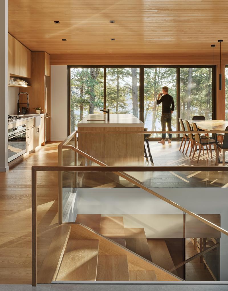 Press kit | 1513-21 - Press release | Long Lake Cottage - Dubbeldam Architecture + Design - Residential Architecture - Expansive wrap-around windows blur the<br>boundaries between indoors and outdoors,<br>enhancing the connection to nature. The<br>warm wood tones of the interior seamlessly<br>frame the view, drawing the surrounding<br>forest into the space.<br> - Photo credit:  Riley Snelling 