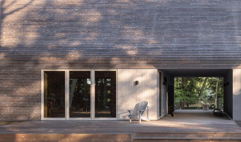 Press kit | 2682-03 - Press release | DogTrot Magnetawan - Williamson Williamson inc - Residential Architecture - Looking through the Dogtrot porch to the forest and lake beyond. The cedar siding covers the entire house from the top of the gable to the foundation. - Photo credit: Scott Norsworthy