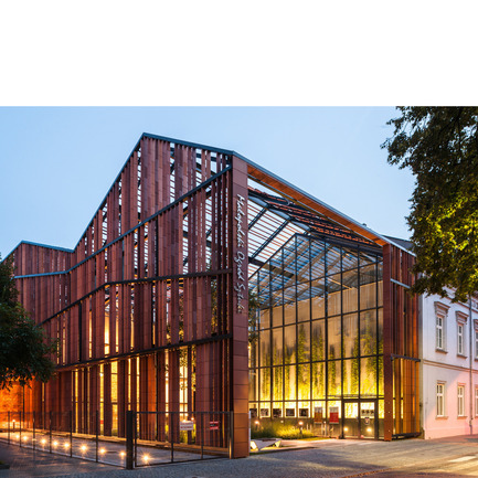 Press kit | 902-02 - Press release | A’ Design Awards 2014 Winners Announced - A' Design Award and Competition - Competition - Malopolska Garden of Arts (MGA)&nbsp;<br>Performing arts centre &amp; mediatheque by Ingarden &amp; Ewý Architects<br><br>PROJECT DESCRIPTION:<br>The building of MGA introduced new spatial order to the old backyards and ruined buildings in Rajska and Szujskiego streets in Krakow. The starting point was a multifunctional hall, which was entered into the outline of the old, 19th-century horse-riding arena, used in the last years of its history as workshops and storage space for the Juliusz Słowacki Theatre in Kraków. The Małopolska Garden of Arts is a cross between two institutions: the Juliusz Słowacki Theatre and the Malopolska Voivodeship Library. The wing on Szujskiego street holds a modern art and media library, with multimedia books and music, while the section standing on Rajska street has been developed by the theatre, and is equipped with a multifunctional events hall. The new hall – operating, as a studio theatre, conference room, concert hall, and venue for banquets and exhibitions – holds retractable stages for 300 people. State-of-the-art stage technology is present overhead: fixed on hoists and cranes to the steel ceiling girders. This allows dramas and concerts to be performed, and exhibitions, film screenings, symposiums, conferences, art auctions, fashion shows, and many more events to be held. Altogether, the space of about 4300 sq.m houses a theatre together with a cosy cinema with 98 seats, a café, and premises for the organisation of educational, art-related activities. Honing the form, the architects focused on interaction with the future recipients, which is why the entire spatial form of the symbolic, openwork roofing raised over the garden from the side of Rajska Street – though not functioning as an actual roof – is there to transport the gateway to the stage out onto the street. In this way, the building delicately nudges passers-by with the skilful manipulation of the form, already at first glance giving the onlooker the impression of going beyond the borders of a garden, where culture is grown in evenly planted rows. Further proof of the sophisticated play with the space is the garden itself. Imitating flower beds, the equal bands with low greens are a metaphor of a garden: as much as the architects could afford here. A notable fact is that historically “ulica Rajska” – literally “Paradise Street” – led to the Garden of Paradise, which was later replaced by the developments of the Tobacco Works. The final impact is the result of the designers’ sensitivity to signals coming from the environment. For example, the opening in the perforated roof of the garden was formed, especially for the maple tree that grows there. In this place, the cultural life of the Kraków’s young artistic set will blossom under a shared roof. Modern ballet, contemporary theatre forms, audio and video arts, concerts, and all and any other artistic pursuits will find their home here. - Photo credit: Marcin Czechowicz / MURATOR ©, 201