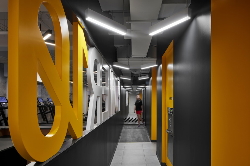 Dossier de presse | 1513-04 - Communiqué de presse | Power10 Fitness - Dubbeldam Architecture + Design - Design d’intérieur commercial -  Connecting the rowing studio and training area with the change rooms is a long corridor with a 3-foot high, three-dimensional POWER10 logo in a 25-foot long opening in the wall that runs behind the reception area, providing a powerful and dynamic visual connection between the spaces.<br>  - Crédit photo : Riley Snelling