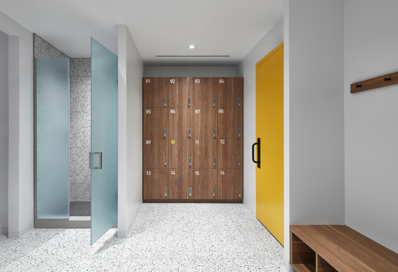 Dossier de presse | 1513-04 - Communiqué de presse | Power10 Fitness - Dubbeldam Architecture + Design - Design d’intérieur commercial -  The sophisticated material palette carries into the change rooms with walnut millwork, terrazzo tiles, frosted glass and a “power gold” hue that is also used throughout the studio.<br>  - Crédit photo : Riley Snelling