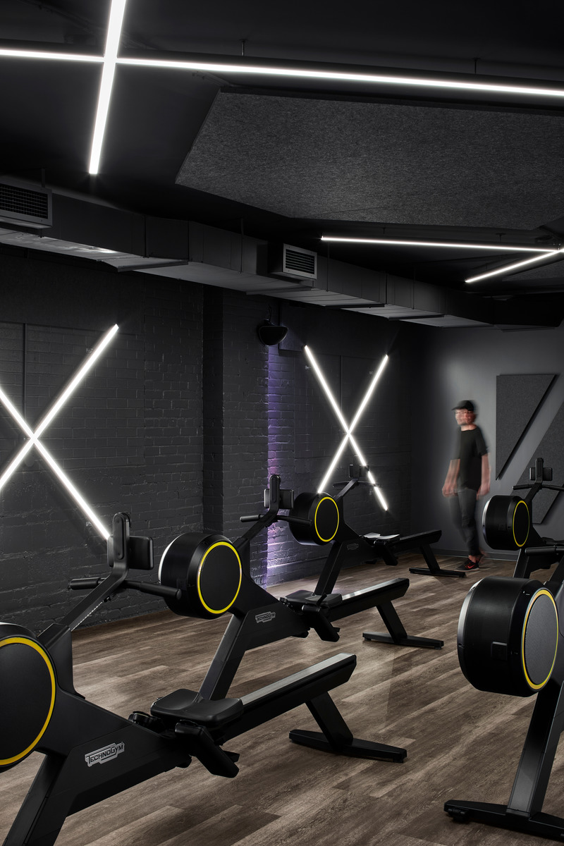 Dossier de presse | 1513-04 - Communiqué de presse | Power10 Fitness - Dubbeldam Architecture + Design - Design d’intérieur commercial -  In the rowing studio, X-shaped LED lighting - alluding to the roman numeral 10 - integrated on the walls and ceiling. During training sessions, colour-changing lights pulsate to the music, adding another layer of intensity to the workout experience.<br>  - Crédit photo : Riley Snelling