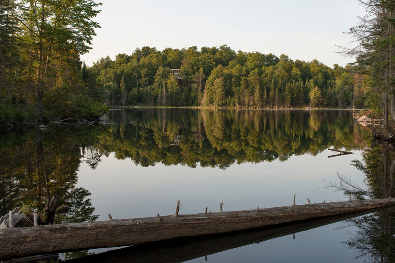 Press kit | 1640-01 - Press release | Territories and Landscapes Exhibition in Paris by Atelier Pierre Thibault - Atelier Pierre Thibault - Event + Exhibition -    Résidence Le Grand Plateau (2014), Laurentians<br>The Grand Plateau site overlooks Lac Heron in the Laurentians and has a striking beauty. The idea of creating a platform from which the view could be fully appreciated while respecting the natural balance of the site became obvious upon first visiting the site. From the arrival, the house presents itself as a generous belvedere offering a direct observation point on the lake below. Accessible from a footbridge linking it delicately to the main path, this large terrace is in fact the roof of the house, which is camouflaged on the lower level. Sober, the spatial arrangement is rigorously articulated according to a structural framework of nine squares acting as a basic grid to the composition and allowing the support on pilings minimizing the impact of the construction on the steep site. The house thus evokes its respect for the fragility and beauty of the landscape that graciously welcomes it.<br>      - Photo credit: Alain Laforest