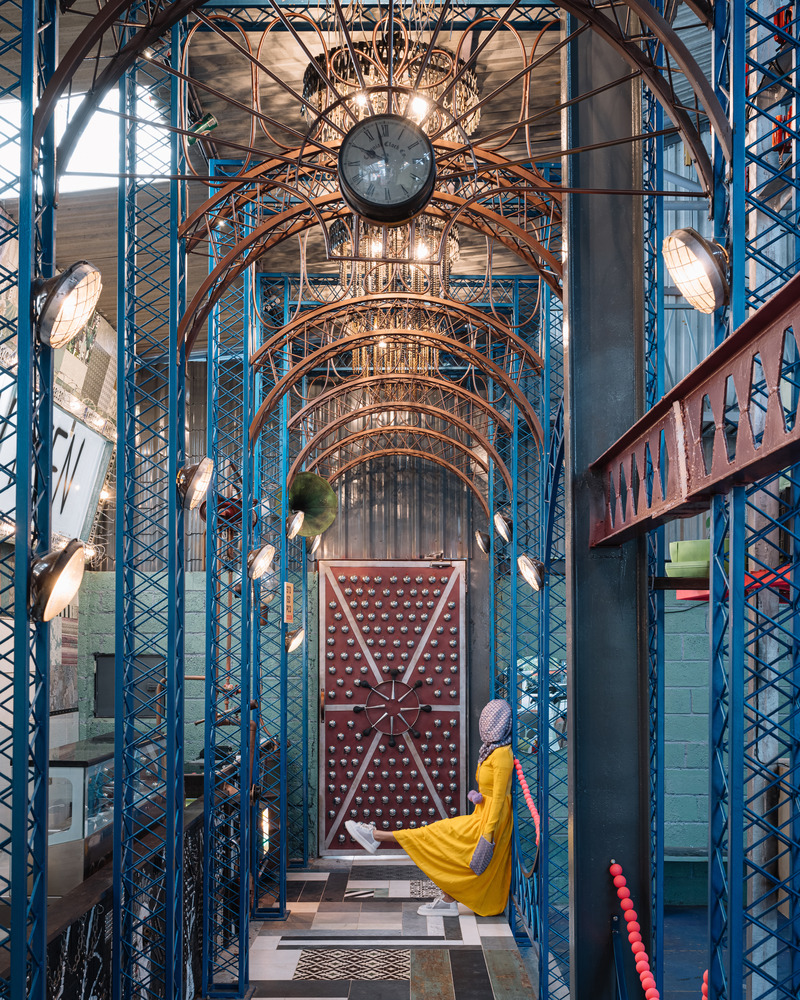 Press kit | 7002-01 - Press release | Big Top - Multitude Of Sins - Commercial Interior Design - <p>A series of arches dot the passage when one makes their way inside. Bathed in a lively warm teal hue, these arches made of scrap metal pose as architectural features to create a sense of movement as one traverses the space. Grunge chandeliers made of bike chains and metal filings levitate over the passageway, flanked by upcycled vehicle headlights that present themselves as bespoke luminaires</p> - Photo credit: Ishita Sitwala