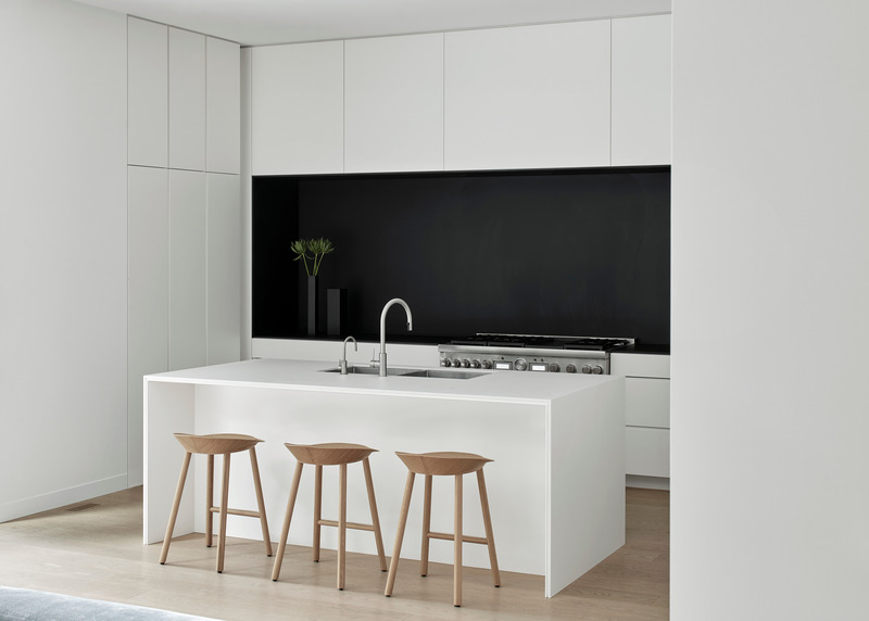 Dossier de presse | 1728-03 - Communiqué de presse | West End Renovation - Akb Architects - Architecture résidentielle - Matte black finishes surrounding the cooking range express a singular recessed volume in an otherwise all-white kitchen. Counter stools by e15.  - Crédit photo : Shai Gil