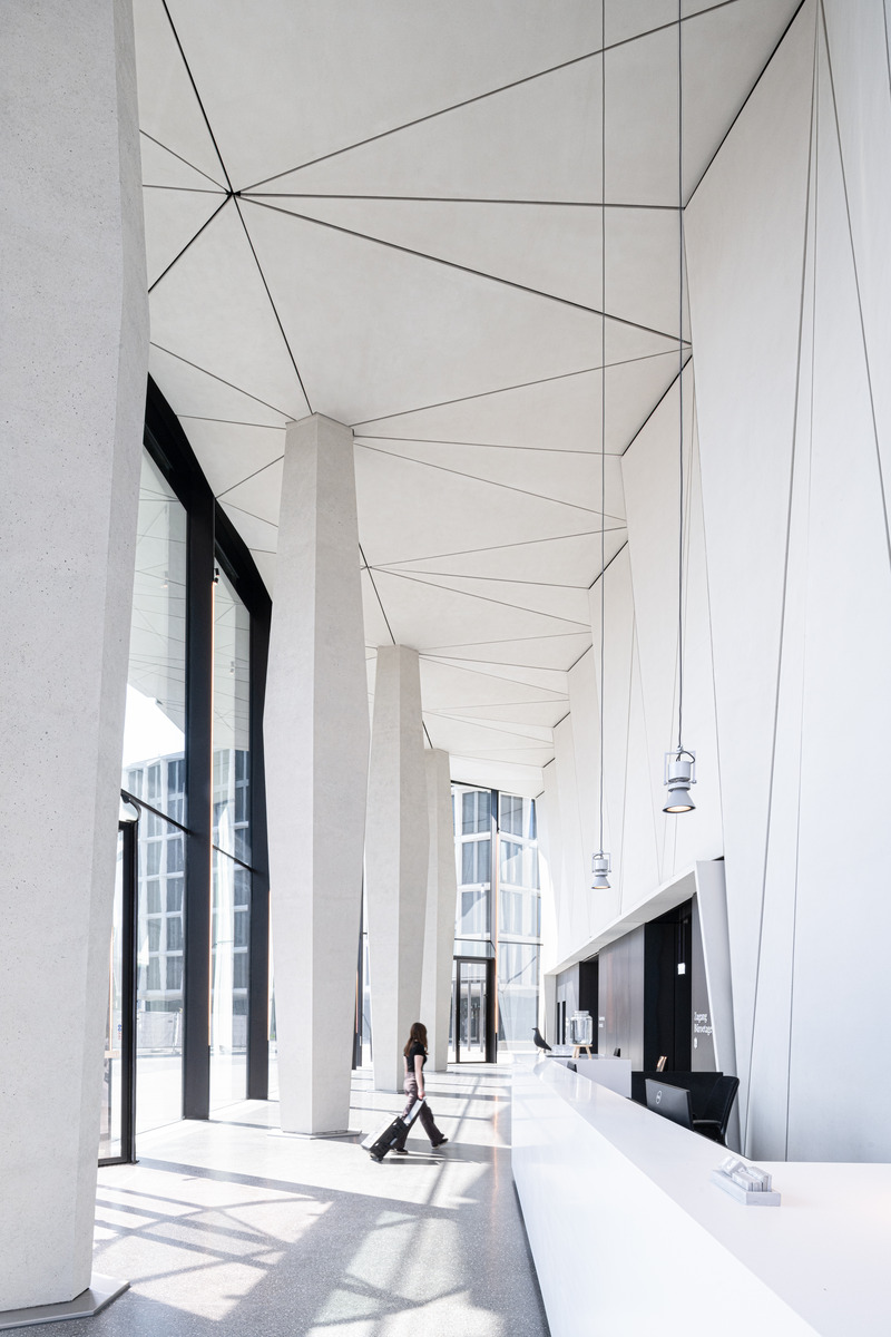 Dossier de presse | 6515-01 - Communiqué de presse | "Neuer Kanzlerplatz" Office Quarter - Bonn, Germany - JSWD - Immobilier -  Entrance hall with slender hinged supports of the high-rise building  - Crédit photo : Christa Lachenmaier