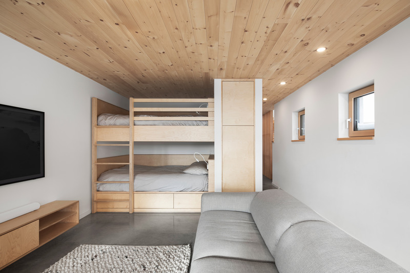 Dossier de presse | 2054-04 - Communiqué de presse | Chalet Papillon - RobitailleCurtis - Architecture résidentielle -  Vue du salon/salle de jeux de l'étage inférieur; vue vers le Nord-Ouest et vue des lits superposés sur mesure en bois d'érable. - Crédit photo :  Adrien Williams 