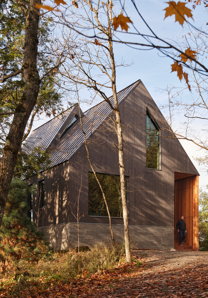 Dossier de presse | 1513-20 - Communiqué de presse | Bunkie on the Hill - Dubbeldam Architecture + Design - Architecture résidentielle - Natural materials were chosen to complement the rustic context. Greyed wood siding contrasts the natural cedar soffits and screen framing the entrance, sitting atop the raw, board-formed concrete base.  <br style=""> - Crédit photo : Riley Snelling