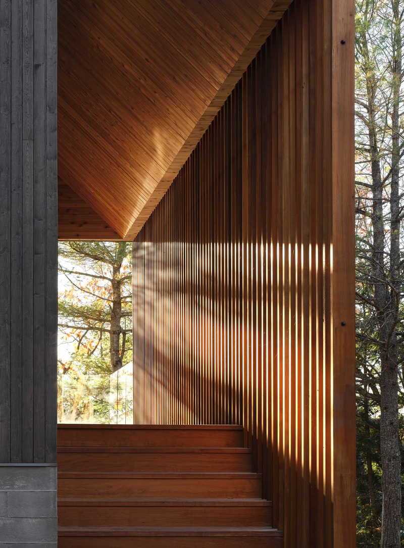 Dossier de presse | 1513-20 - Communiqué de presse | Bunkie on the Hill - Dubbeldam Architecture + Design - Architecture résidentielle - The slatted screen echoes the tree trunks seen through framed views at each end. The cedar slats are animated by the ever-changing west light that filters through its openings, producing a dynamic interplay of light and shadows. - Crédit photo : Riley Snelling