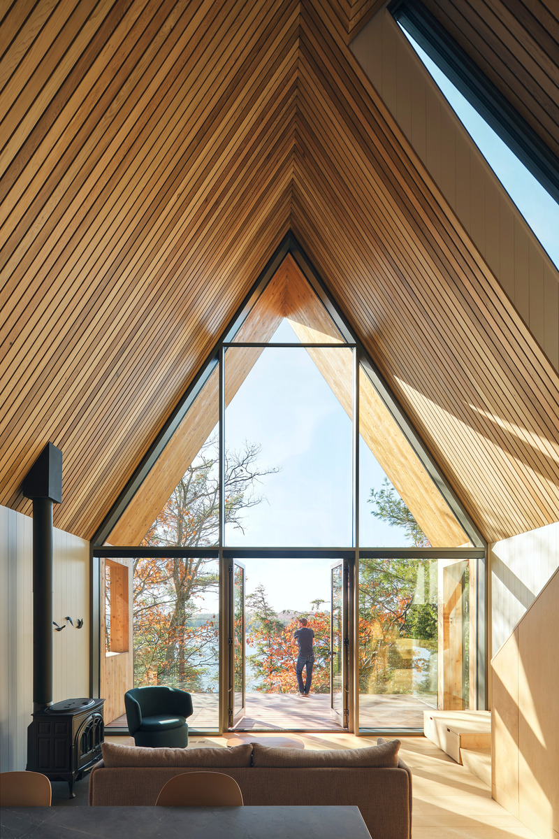 Dossier de presse | 1513-20 - Communiqué de presse | Bunkie on the Hill - Dubbeldam Architecture + Design - Architecture résidentielle - A contemporary interpretation of the traditional A-frame shape, the lofted ceiling is delineated with Western red cedar boards. The living area features stunning views of the lake below through a triple-glazed opening. - Crédit photo : Riley Snelling
