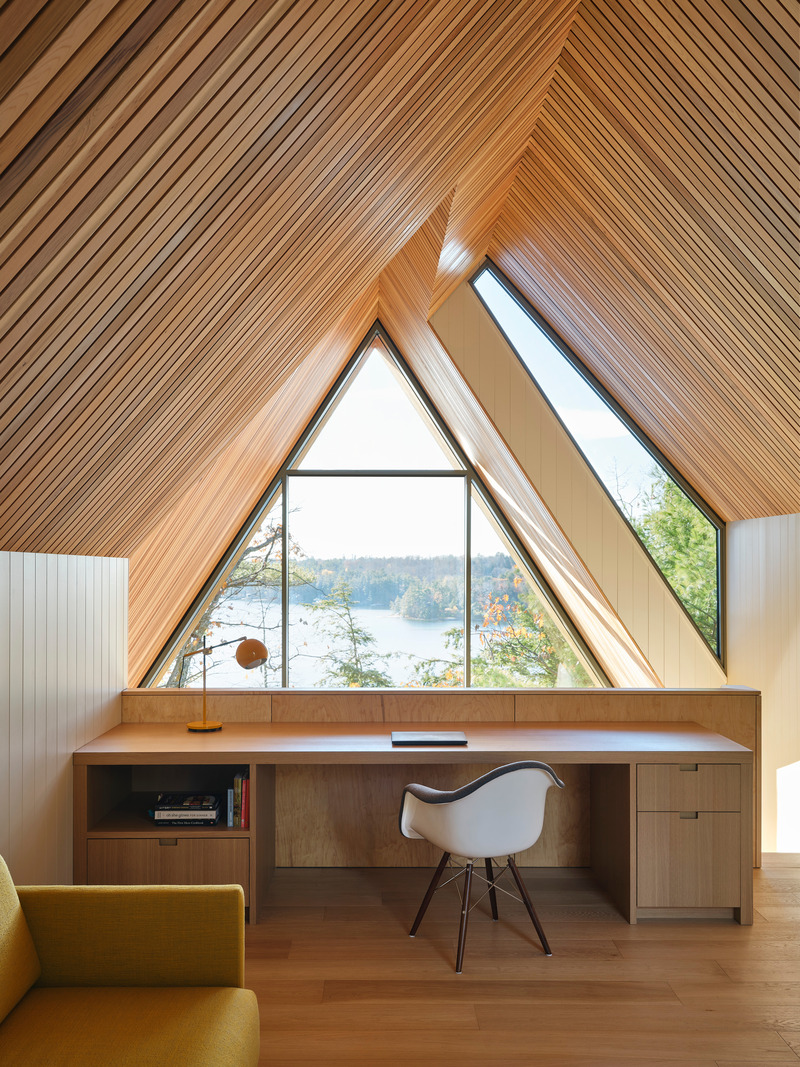 Dossier de presse | 1513-20 - Communiqué de presse | Bunkie on the Hill - Dubbeldam Architecture + Design - Architecture résidentielle - The split roof design features two intersecting gables that create opportunities for window openings where the roof volumes separate, seen at eye-level from the upper loft. A built-in desk features views down to the living space on the first level and the lake beyond. - Crédit photo : Riley Snelling