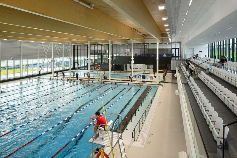 Press kit | 3253-05 - Press release | The Saint-Georges Multisport Complex: Bright and Welcoming - ABCP architecture in consortium with MLL et BBL architects - Institutional Architecture - The semi-Olympic pool area with its 250-seat bleachers overlooking the high school sports field and bay windows protected by the canopy. - Photo credit: Stéphane Groleau