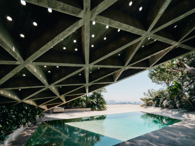 Dossier de presse | 2757-45 - Communiqué de presse | Honoring Architectural Lineage: Conner + Perry Architects Usher in a New Phase for an LA Landmark - Conner + Perry Architects - Architecture résidentielle - <p class=""><b>Sheats-Goldstein Residence:</b> View stepping out from the living room onto the pool deck wrapped in pebble finished concrete. The powerful yet light triangulated concrete coffered roof structure hangs overhead, punctuated with tiny skylights that allow the sunlight to dapple through. The zero edge of the pool sits flush to the surface of the deck and was the first of its kind in the United States. </p> - Crédit photo : Joe Fletcher Photography